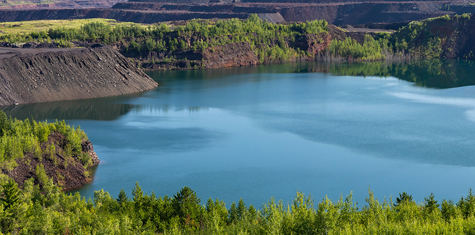 Blue water lake surrounded by dirt cliffs and green tree forest