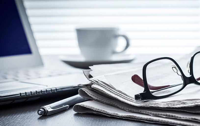 Laptop coffee cup, reading glasses on pile of newspapers