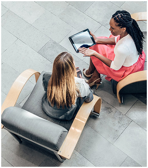 Two woman sitting in chairs having a discussion over a tablet