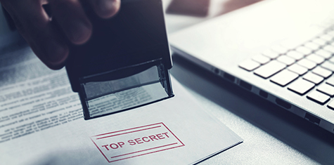 Hand stamping "Top Secret" on document next to a laptop