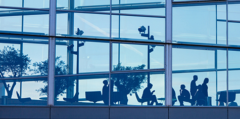 Multiple people in an open office area seen through skyskraper windows