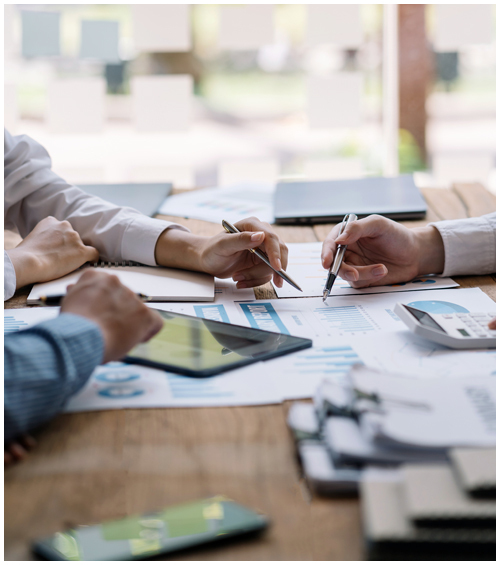 Hands of multiple people working at a table covered with multiple documents and a tablet